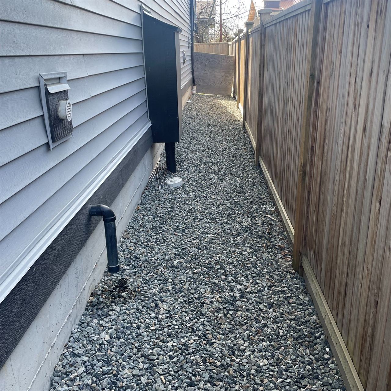 Gravel side-yard strip with drainage beside a cedar fence