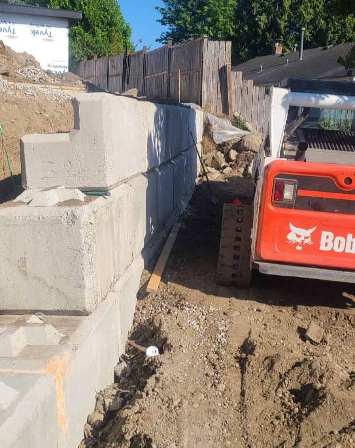 Concrete lock-block retaining wall built alongside a Bobcat skid steer